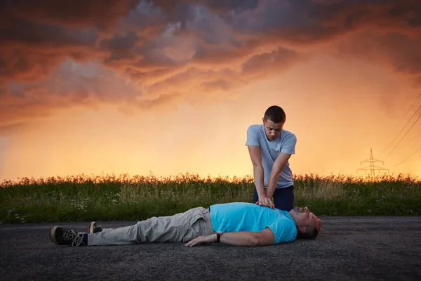 도로에서의 청년은 아래서 의식을 남자를 치료하고 — 스톡 사진
