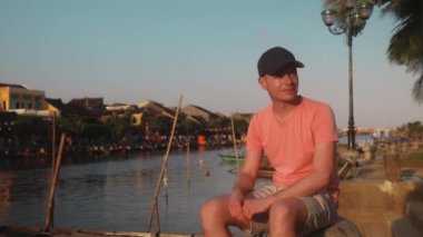 Geleneksel fenerlerle süslenmiş eski kasabanın rıhtımında oturan gezgin. Adam antik şehir Hoi An 'a bakıyor, Vietnam' a. 4K çözünürlükte gerçek zamanlı. 