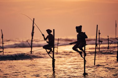 Alacakaranlıkta okyanusa karşı iki geleneksel balıkçının siluetleri. Sri Lanka 'da Galle yakınlarında geleneksel balık avı