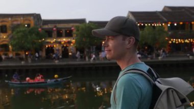 Geleneksel fenerlerle süslenmiş eski kasabanın rıhtımını ziyaret eden gezgin. Adam antik şehir Hoi An 'a bakıyor, Vietnam' a. 4K çözünürlükte gerçek zamanlı. 