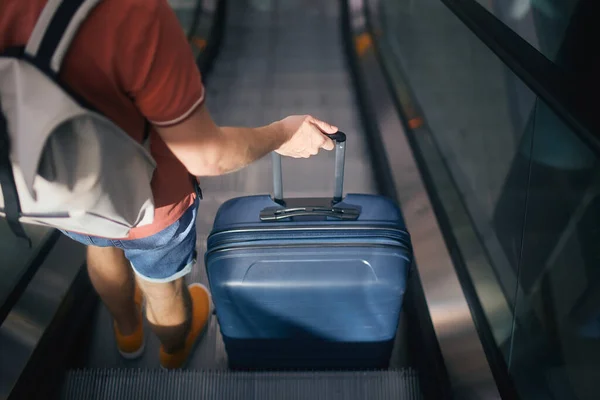 旅行者は空港ターミナルを歩く エカレーターにスーツケースとバックパックを持った男のリアビュー 乗客は旅行の準備ができています — ストック写真