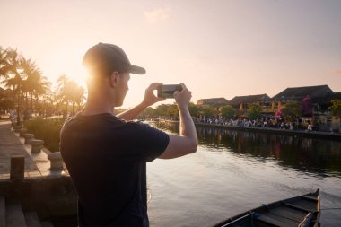 Hoi An şehir manzarasını fotoğraflayan adam. Güzel günbatımında antik şehirde akıllı telefonlu bir turist, Vietnam