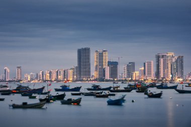 Alacakaranlıkta Da Nang şehir manzarası. Limana demirlemiş balıkçı teknesi modern binalarla aydınlanmış kıyılara karşı.