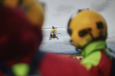 Yaklaşan acil tıbbi servis helikopterine bakarken kask takan sağlık görevlilerinin arka görüntüsü. Tema kurtarma, acil durum ve sağlık hizmetleri