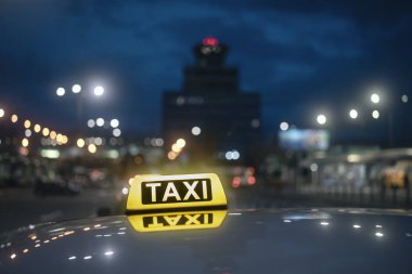 Sarı taksi işaretine odaklan. Geceleri havaalanı terminaline karşı arabanın çatısında yansıma..