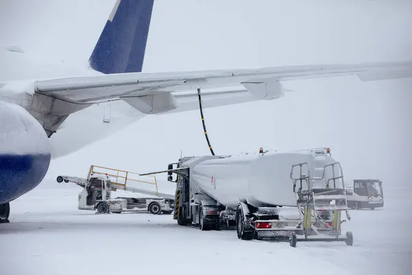 Refueling of airplane from fuel tanker truck at airport during snowfall. Ground service before flight on frosty winter day.