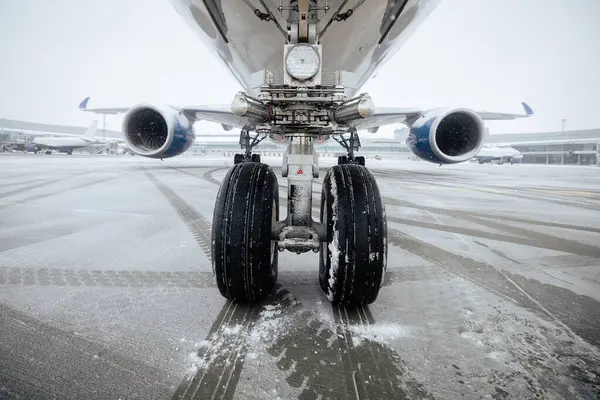 Front view of airplane landing gear. Winter frosty day at airport during snowfall.
