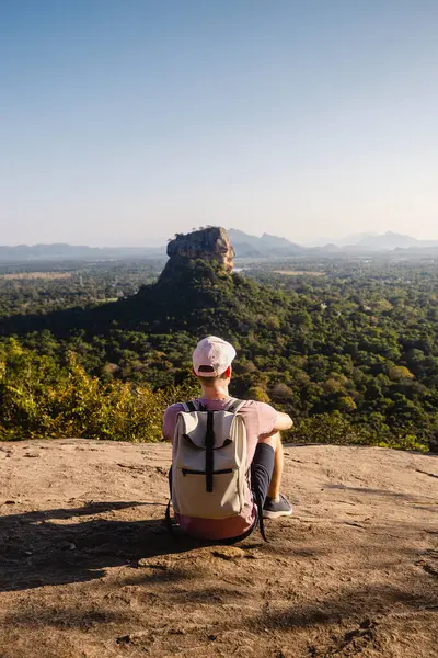 背着背包坐在岩石上看风景的男人 美丽的风景与Sigiriya岩石 在斯里兰卡的单身旅行者 免版税图库图片