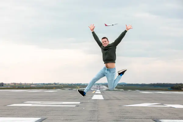 喜びと気楽な旅行のコンセプト 空港滑走路でジャンプする腕を持つ幸せな男 ストック画像