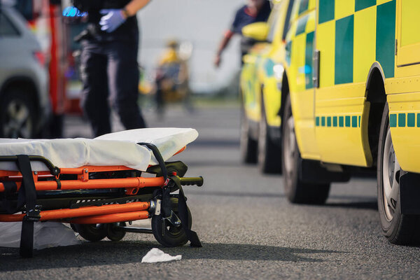 Selective focus on stretcher against ambulance cars of emergency medical service, firefighters and rescue helicopter on road. Themes rescue, urgency and health care.