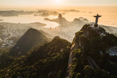 Rio de Janeiro, Brazil - March 21, 2023: Christ the Redeemer statue on top of the Corcovado Mountain with the Sugarloaf Mountain in the  horizon on sunrise. clipart