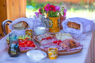 Taze ekmek, süt, sebze, çatal bıçak ve çiçek dekoru içeren renkli bir kahvaltı..