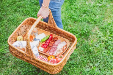 Açık havada içi dolu bir piknik sepeti taşıyan, lezzetli atıştırmalıklar sunan bir elin yakın çekimi..
