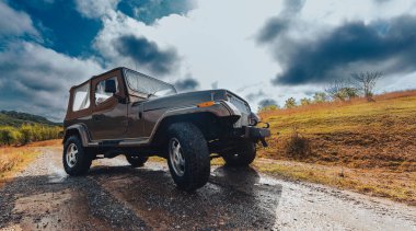 Bulutlu bir gökyüzünün altında toprak bir yolda giden engebeli bir off-road aracı..