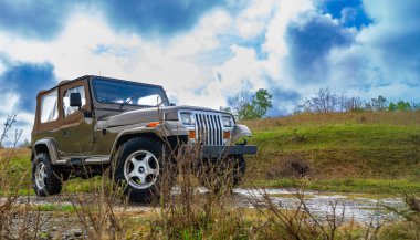 Çarpıcı bulutlu bir gökyüzünün altındaki yemyeşil bir yamaçta engebeli bir off-road aracı..