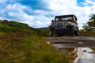 Yeşil tepelerin ve bulutlu gökyüzünün yakınındaki kırsal bir yolda park edilmiş engebeli bir off-road aracı..