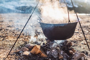 Bir dökme demir tencere ateşin üzerinde asılı, kırsal bir yerde dışarıda yemek pişiriyor..