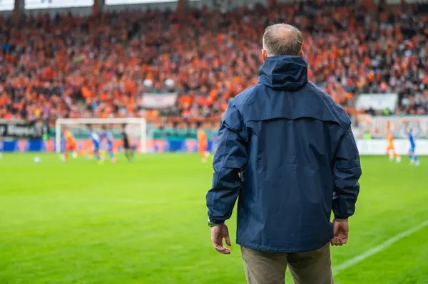 Head coach's back and soccer match at the stadium in the background