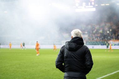 Baş antrenör döndü ve arka plandaki stadyumda futbol maçı var..