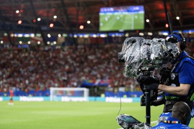 Adam futbol stadyumundaki dengeleyicide televizyon kamerası taşıyor.