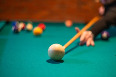 Yeşil bir bilardo masasında beyaz bilardo topuna vuran kişi.