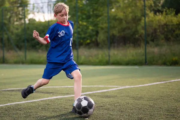 Yuong çocuk sahada suni çimlerle topa vuruyor.