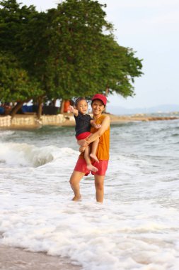 Anne çocuğunu kucağında tutuyor ve plajda oynuyor anne ve çocuk, Tayland 'ın tropikal deniz sahillerinde oyun oynuyorlar..