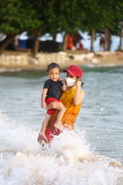 Anne çocuğunu kucağında tutuyor ve plajda oynuyor anne ve çocuk, Tayland 'ın tropikal deniz sahillerinde oyun oynuyorlar..