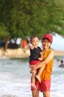 Anne çocuğunu kucağında tutuyor ve plajda oynuyor anne ve çocuk, Tayland 'ın tropikal deniz sahillerinde oyun oynuyorlar..