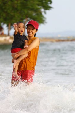 Anne çocuğunu kucağında tutuyor ve plajda oynuyor anne ve çocuk, Tayland 'ın tropikal deniz sahillerinde oyun oynuyorlar..