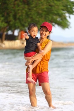 Anne çocuğunu kucağında tutuyor ve plajda oynuyor anne ve çocuk, Tayland 'ın tropikal deniz sahillerinde oyun oynuyorlar..