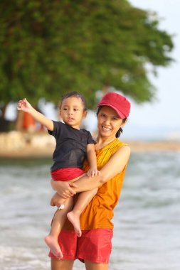 Anne çocuğunu kucağında tutuyor ve plajda oynuyor anne ve çocuk, Tayland 'ın tropikal deniz sahillerinde oyun oynuyorlar..