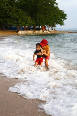 Anne çocuğunu kucağında tutuyor ve plajda oynuyor anne ve çocuk, Tayland 'ın tropikal deniz sahillerinde oyun oynuyorlar..
