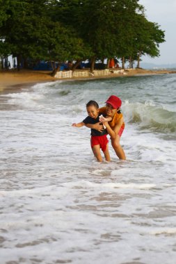 Anne çocuğunu kucağında tutuyor ve plajda oynuyor anne ve çocuk, Tayland 'ın tropikal deniz sahillerinde oyun oynuyorlar..
