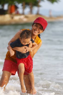Anne çocuğunu kucağında tutuyor ve plajda oynuyor anne ve çocuk, Tayland 'ın tropikal deniz sahillerinde oyun oynuyorlar..