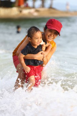 Anne çocuğunu kucağında tutuyor ve plajda oynuyor anne ve çocuk, Tayland 'ın tropikal deniz sahillerinde oyun oynuyorlar..