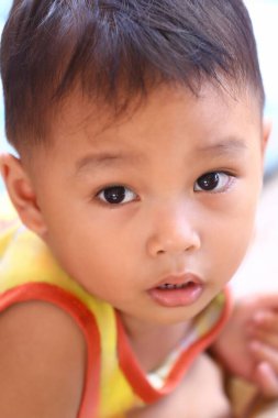 İki yaşlarında, sarı tişörtlü Asyalı bir çocuk oturmuş tuhaf bir şekilde bir şeye bakıyordu..