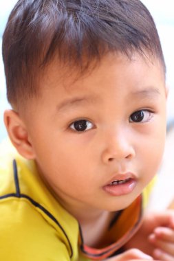 İki yaşlarında, sarı tişörtlü Asyalı bir çocuk oturmuş tuhaf bir şekilde bir şeye bakıyordu..