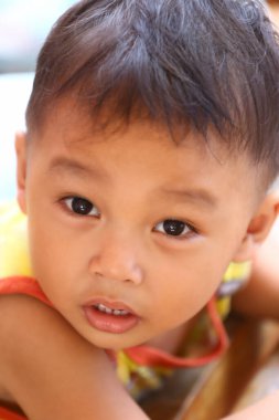 İki yaşlarında, sarı tişörtlü Asyalı bir çocuk oturmuş tuhaf bir şekilde bir şeye bakıyordu..