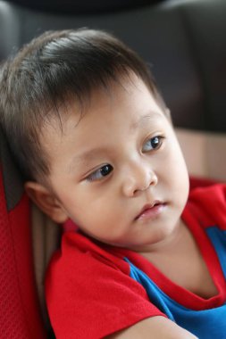Asyalı bir çocuk bir araba koltuğunda oturur ve dışarı bakar, bir şeyle ilgilenir..