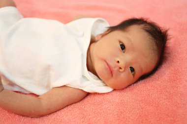 Yeni doğmuş bir bebek gözleri açık, kırmızı bir yatak ve beyaz bir gömlek giyer.