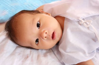 Beyaz tişörtlü bir çocuk beyaz bir yatakta mutlu bir şekilde yatıyor..