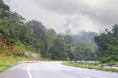 Dağların arasından geçen yol bomboştu ve sabah sis vardı. Yolun her iki tarafı da yeşil ağaçlarla doluydu. Arka planda beyaz bulutlar vardı..