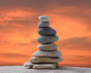 Günbatımında bir arkaplanda piramit şeklinde istiflenmiş taşlar ve çalışma, seyahat veya zen temasında tasarım için alanı kopyalamak.