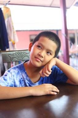 Düşünceli bir çocuk bir masada oturur, çenesini elinde dinlendirir, dalgın dalgın dalgın dalgın dalgın. Bu rahat iç mekan portresi masumiyeti ve merakı yakalıyor..