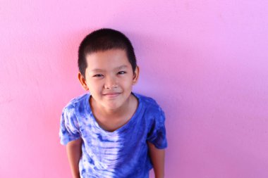 Neşeli bir çocuk canlı pembe bir duvarın önünde neşeli bir şekilde gülümsüyor, genç masumiyetini ve günlük kravat boyası gömleğiyle neşeli bir ruhunu sergiliyor..