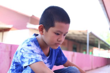 A thoughtful young boy sits alone outdoors, lost in contemplation. His serious expression and casual attire reflect a moment of calm and focus in a vibrant environment. clipart