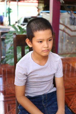 Genç bir çocuk sakin bir ortamda sessizce oturur, sakin bir ifadeyi yansıtır. Doğal ışık, onun düşünceli davranışlarını vurguluyor, çocukluk anını yakalıyor..