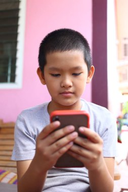 Genç çocuk, modern çocukluğu ve teknolojinin günlük hayattaki rolünü gösteren canlı bir açık hava ortamında akıllı telefonuyla yoğun bir şekilde meşgul..