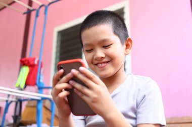 Mutlu bir çocuk akıllı telefonuna bakarken gülümsüyor, dışarıdaki anın tadını çıkarıyor. Parlak arka plan neşeli ve neşeli atmosfere ekleniyor..